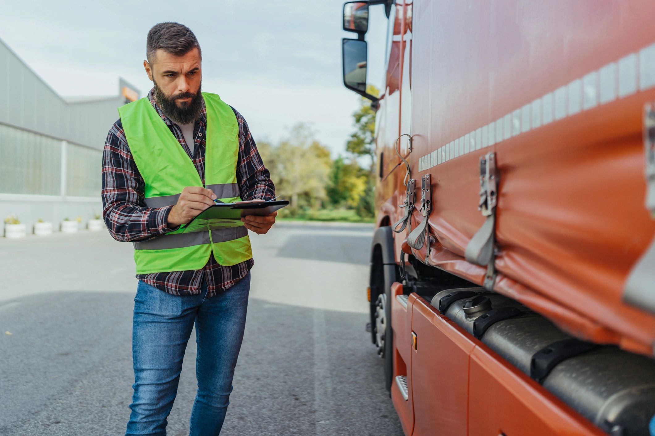 Truck driver checking shipping documents beside a freight truck